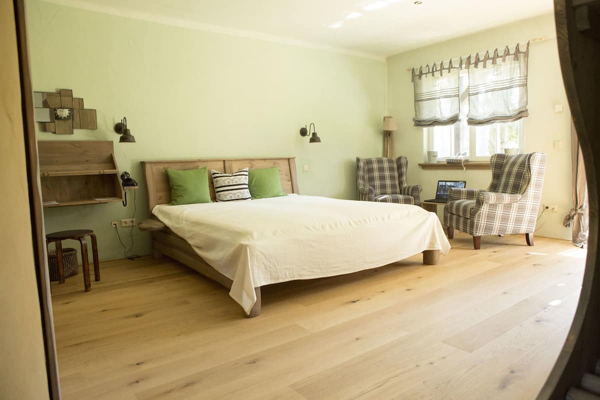Une chambre à coucher avec un lit, deux chaises, un bureau et une fenêtre avec des rideaux.