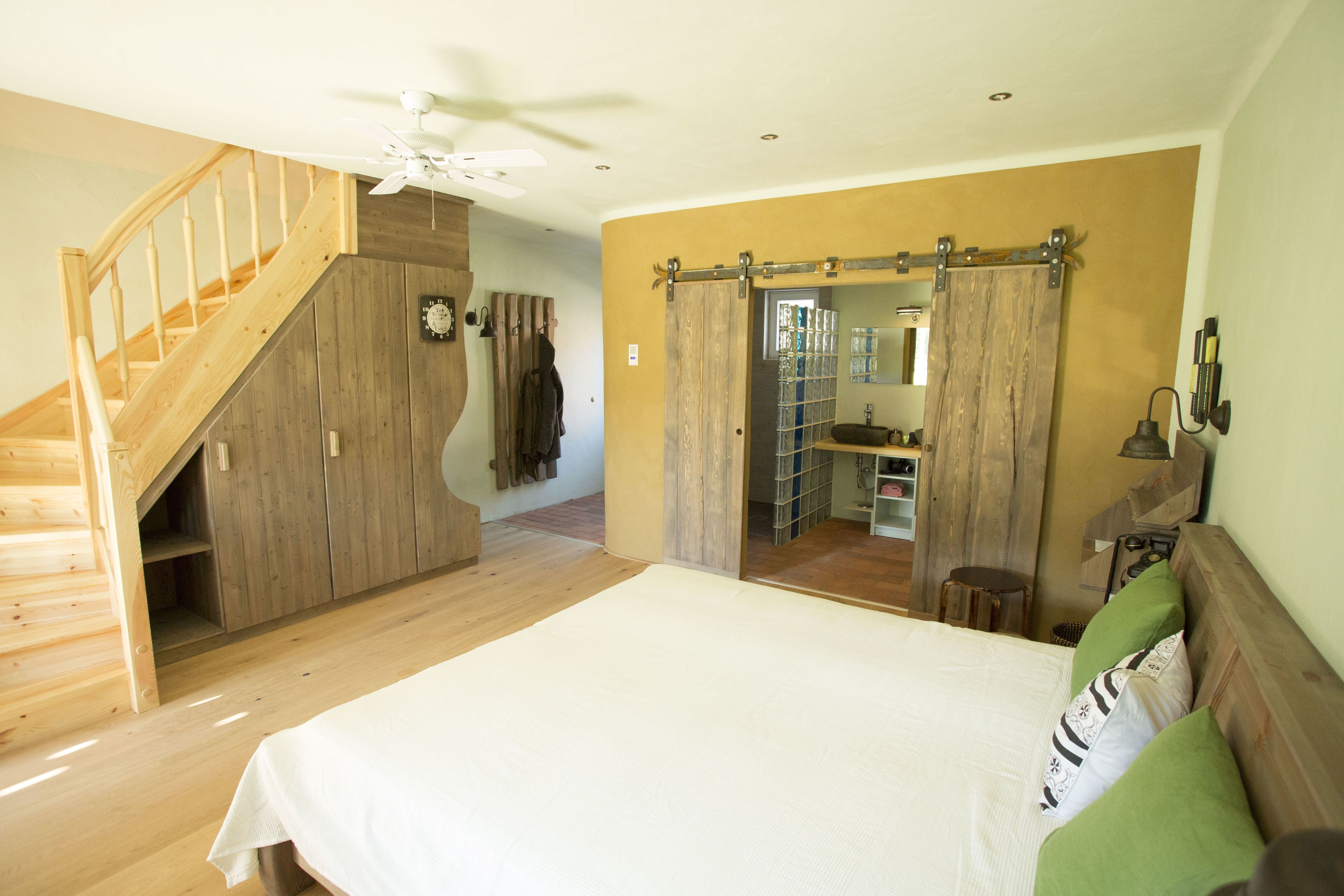 Ein Schlafzimmer mit einer Holztreppe, einem großen Bett und einem durch eine Schiebetür erreichbaren Badezimmer.