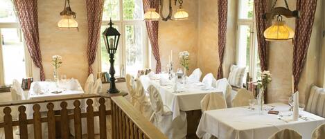 A dining area with multiple tables set for a meal, each with white tablecloths, chairs, and centerpieces.