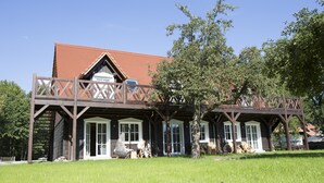 A wooden cabin with a balcony, large windows, and a red roof. - Hotel Kolonieschänke (Burg (Spreewald))