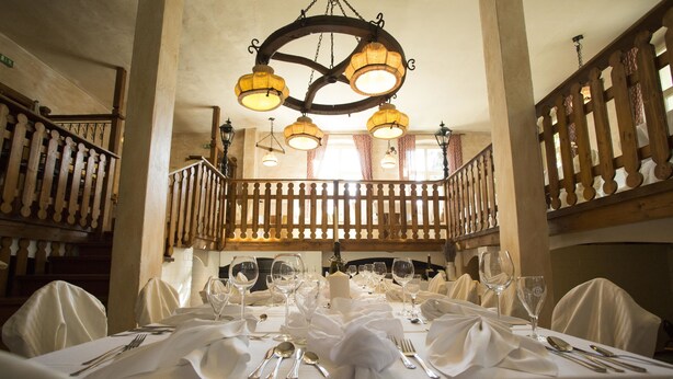 A dining area with a long table set for a meal, surrounded by chairs with white covers, and a wooden railing in the background. - Hotel Kolonieschänke (Burg (Spreewald))