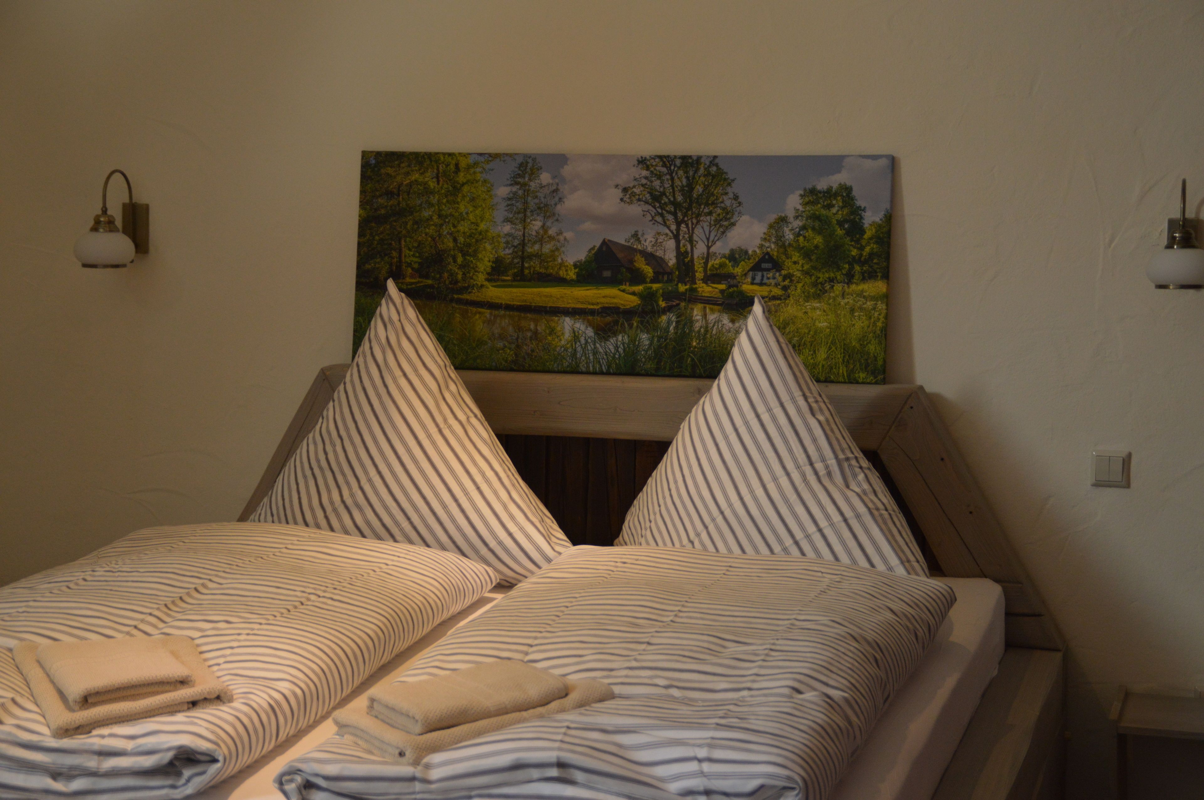 A bedroom with two beds, striped bedding, and a landscape painting above the beds.