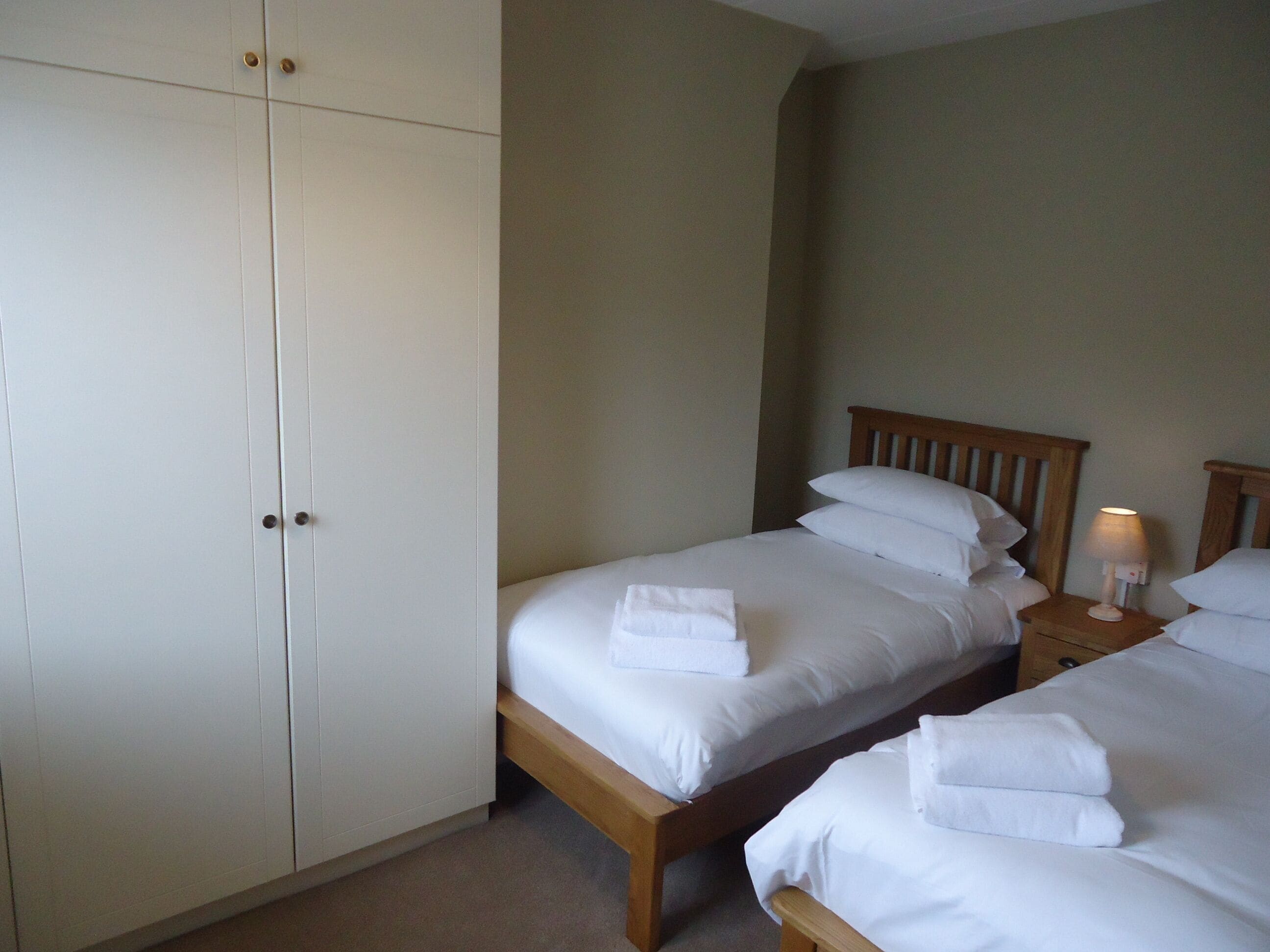 Ein Hotelzimmer mit zwei Einzelbetten, einem Kleiderschrank und einem Nachttisch mit Lampe.