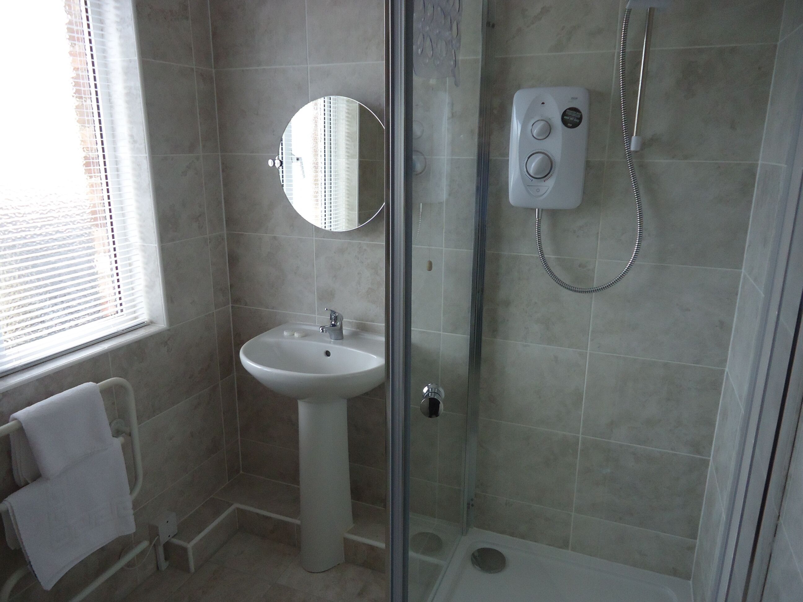 A bathroom with a glass-enclosed shower, a sink with a mirror above it, and a towel rack.