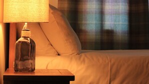 Una cama con edredón blanco y una mesita de noche de madera con lámpara y botella transparente.