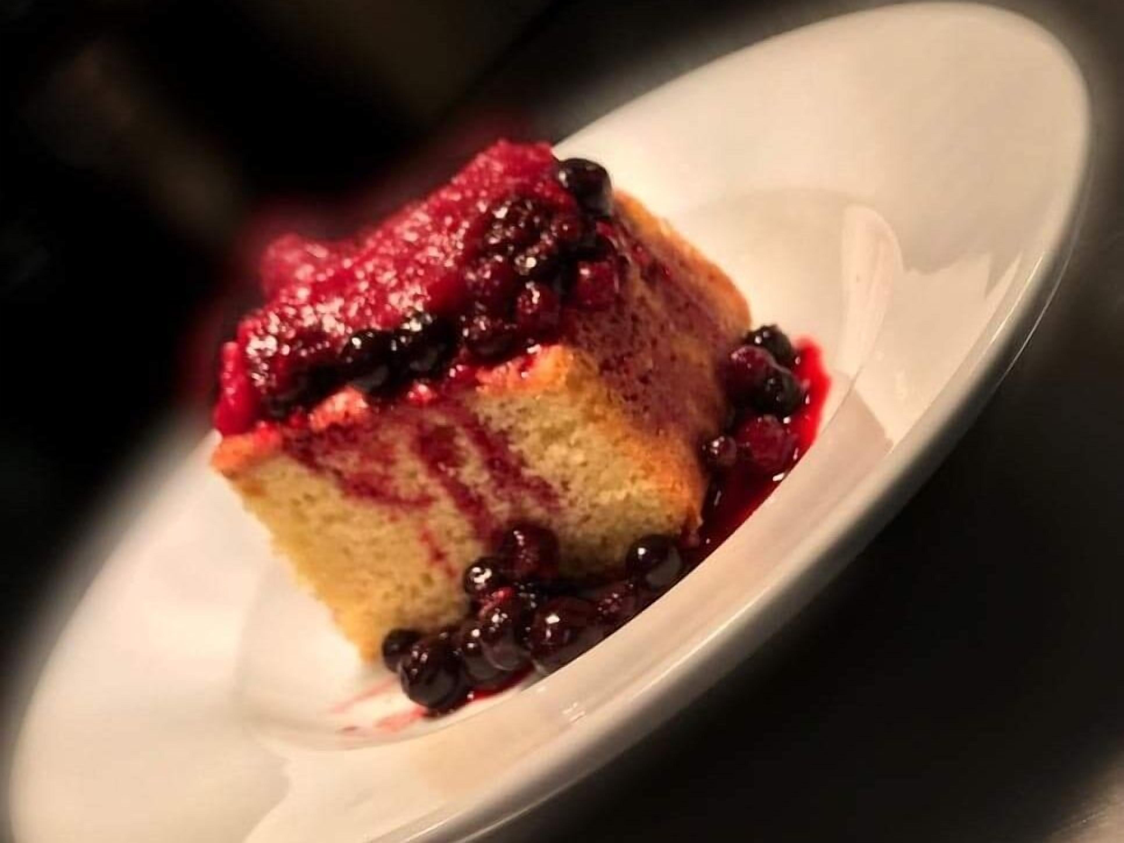 Una porción de pastel con cobertura de frutos rojos sobre un plato blanco.