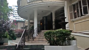 Un edificio con un balcón curvo, una escalera que conduce a la entrada y plantas en macetas alrededor.