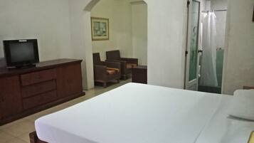 A hotel room with a bed, a TV on a dresser, a chair, and a door leading to a bathroom.