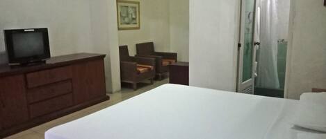 Habitación de hotel con cama, televisor en una cómoda, una silla y una puerta que da a un baño.