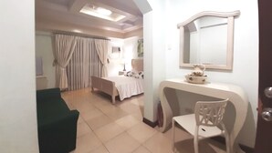 Habitación de hotel con cama, escritorio, silla, tocador con espejo y baño con cortina de ducha.