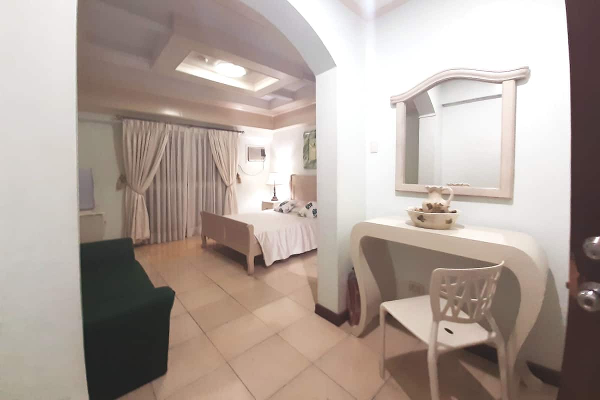 A hotel room with a bed, a desk, a chair, a vanity with a mirror, and a bathroom with a shower curtain.