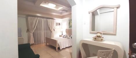Habitación de hotel con cama, escritorio, silla, tocador con espejo y baño con cortina de ducha.
