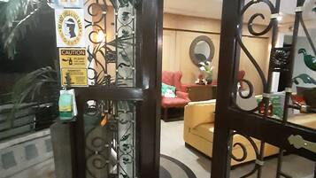 A lobby area with a wet floor sign, a metal gate with decorative patterns, and a red chair in the background.