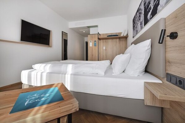 A modern hotel room with a bed, a wooden nightstand, a wall-mounted TV, and a framed picture. - Ecome Hotel (Heidenheim an der Brenz)