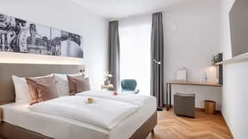 A modern hotel room with a large bed, a desk, and a chair. There is a painting on the wall and a window with curtains.