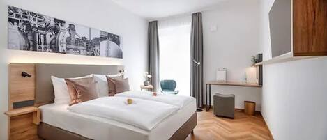 Una habitación de hotel moderna con una cama grande, un escritorio y una silla. Hay un cuadro en la pared y una ventana con cortinas.