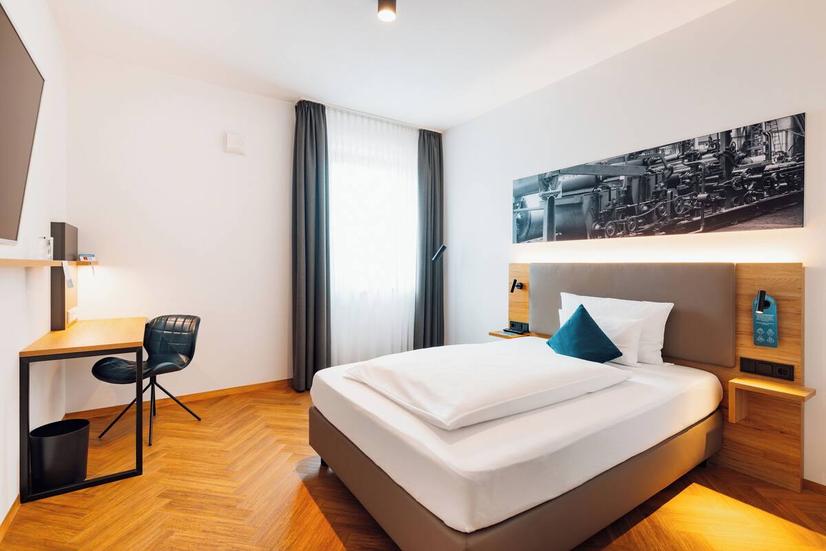 A modern hotel room with a bed, a desk, and a chair.