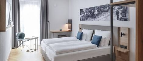 A modern hotel room with a large bed, a desk, and a chair.