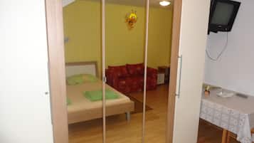 Une chambre à coucher avec un lit, un canapé rouge, une petite table et un téléviseur fixé au mur.