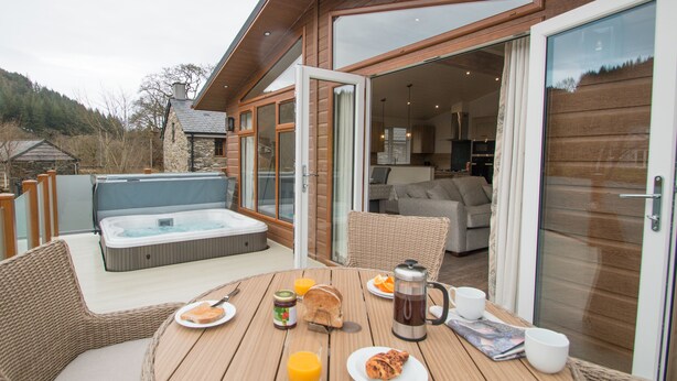 A wooden deck with a hot tub, wicker furniture, and breakfast items. - Hendre Rhys Gethin (Betws-Y-Coed)