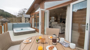 A wooden deck with a hot tub, wicker furniture, and breakfast items. - Hendre Rhys Gethin (Betws-Y-Coed)