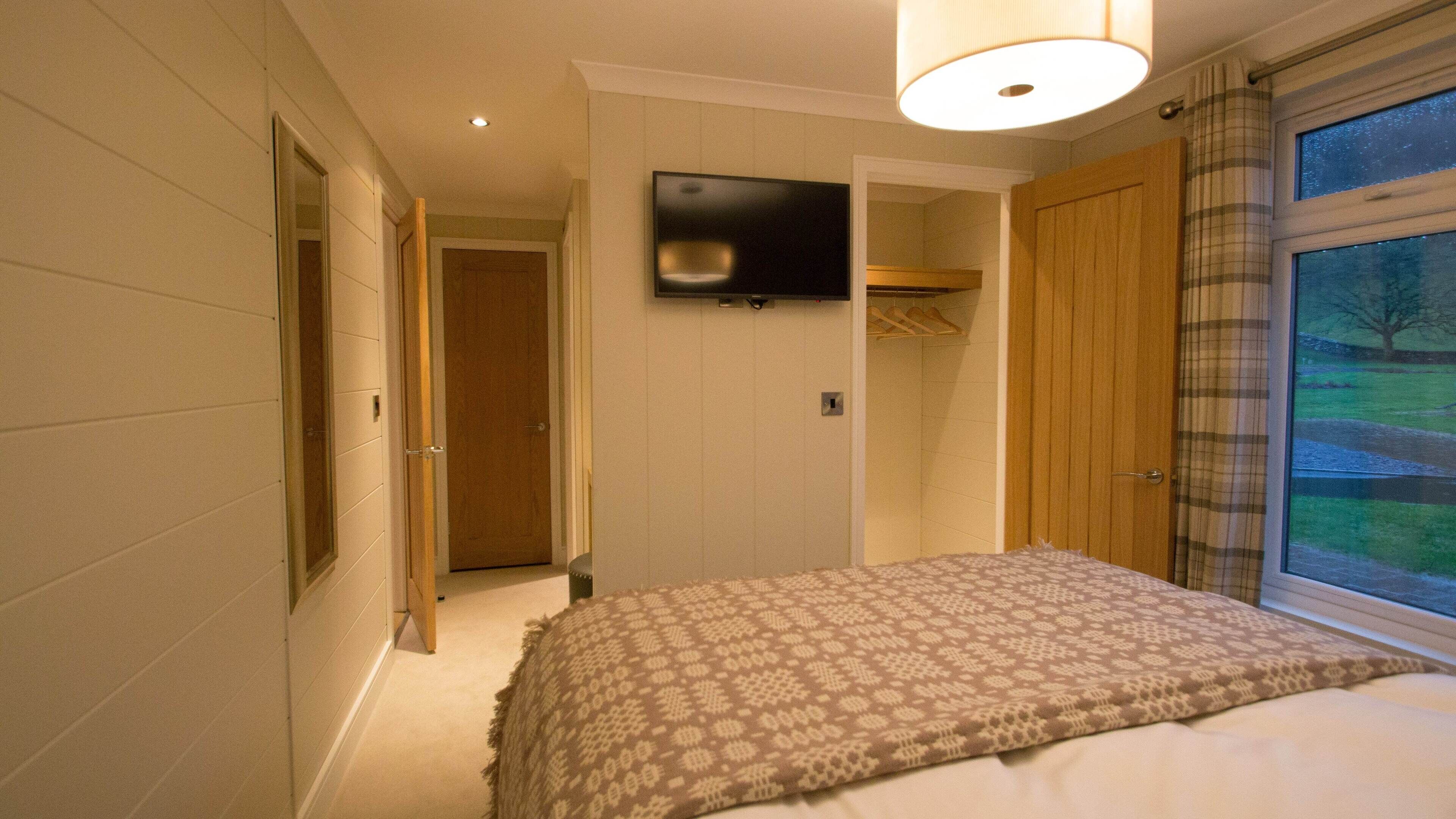 Quarto com cama, televisão na parede e janela com cortinas.