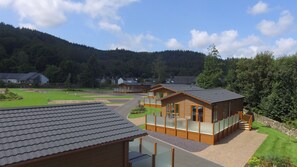 A lodge with a spacious patio, wooden cabins, and a view of a forested hillside. - Hendre Rhys Gethin (Betws-Y-Coed)