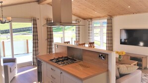 A modern kitchen with a central island, a dining area with chairs, and a TV mounted on the wall. - Hendre Rhys Gethin (Betws-Y-Coed)