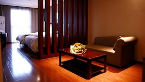 A hotel room with a wooden floor, a bed with white bedding, a sofa, a small table with a fruit basket, and a partition with vertical slats. - GreenTree Inn Jinan Gaoxin District International Convention Centre Hotel (Jinan)