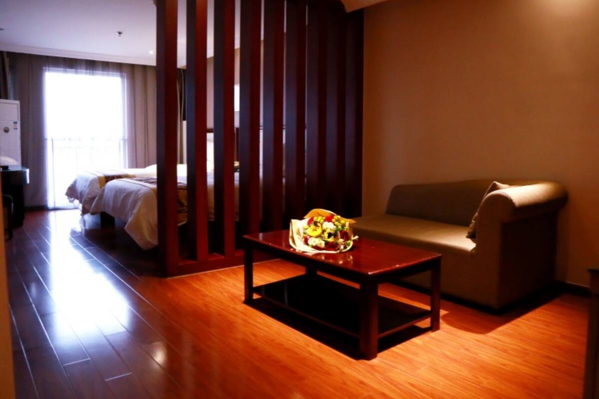 Habitación de hotel con piso de madera, una cama con ropa blanca, un sofá, una mesita con frutera y un separador con listones verticales.