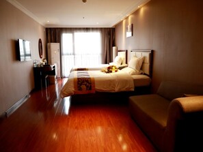 Quarto de hotel com uma cama grande, mesa de cabeceira, escrivaninha, cadeira e televisão.