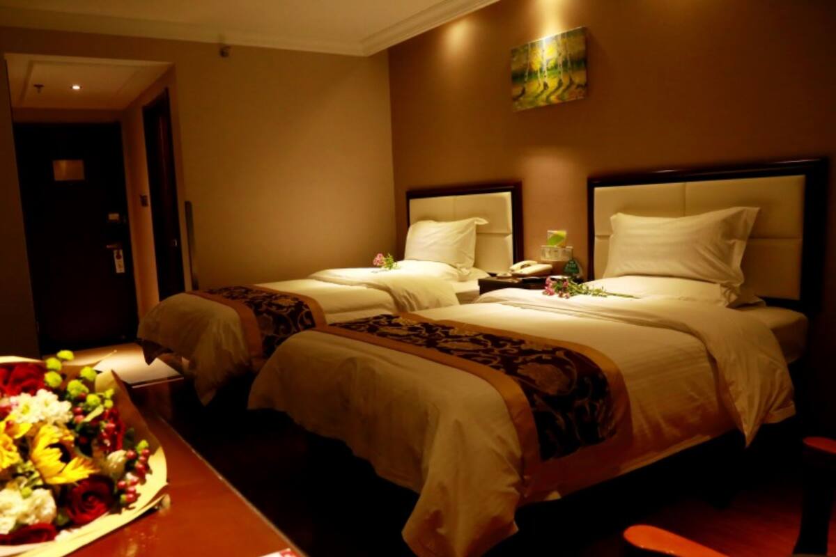 Una habitación de hotel con dos camas, una mesita de noche de madera, una mesa con un ramo de flores y un cuadro en la pared.