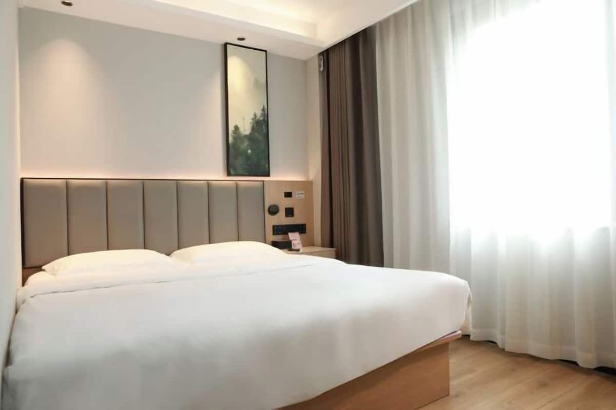 Ein Hotelzimmer mit einem großen Bett, einem Kopfteil mit integrierter Beleuchtung, einem Nachttisch mit Telefon und einem fensterbündigen Vorhang.