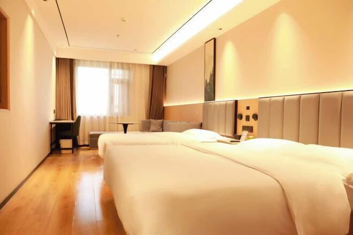 Ein Hotelzimmer mit zwei Betten, einem Schreibtisch, einem Stuhl und einem großen Fenster mit Vorhängen.