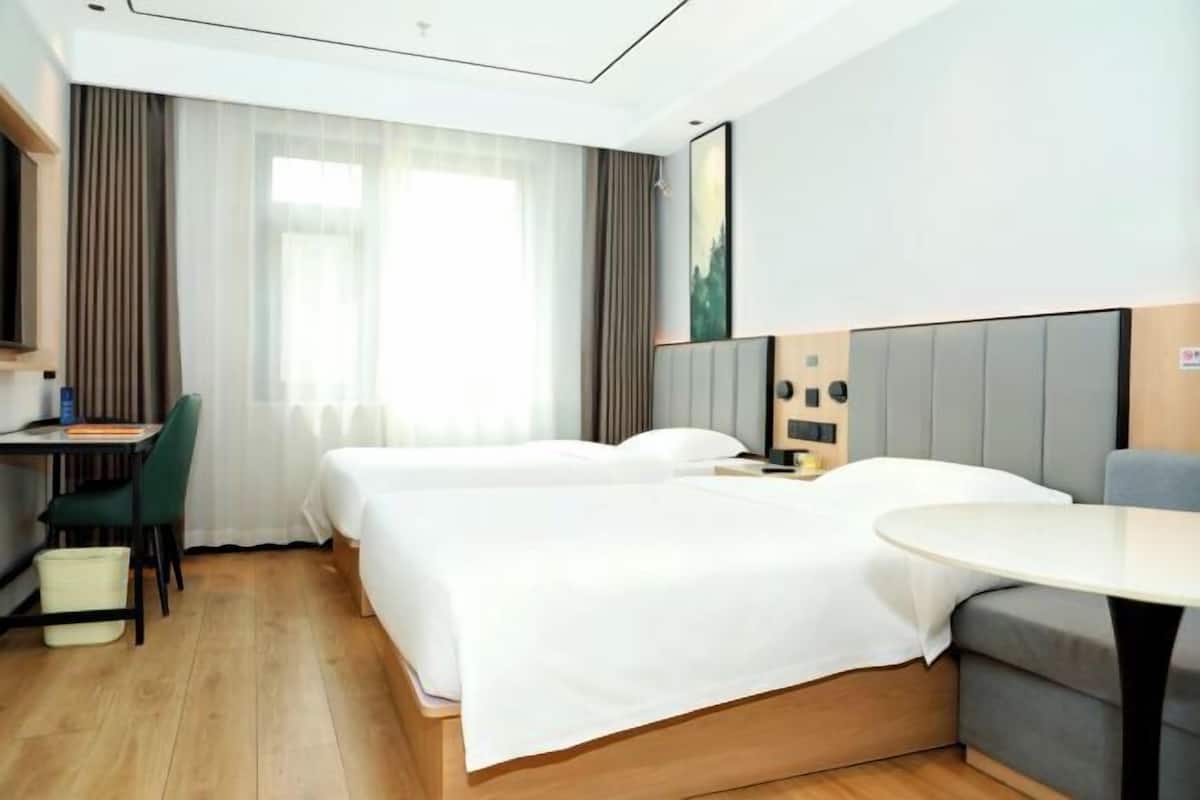 Ein Hotelzimmer mit zwei Betten, einem Schreibtisch, einem Stuhl, einem runden Tisch und einem großen Fenster mit Vorhängen.