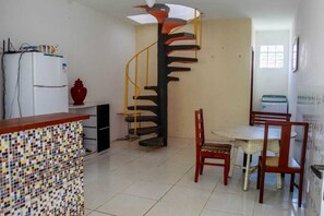 Een keuken met betegelde vloer, een koelkast, een fornuis, een spoelbak, een eettafel met stoelen en een spiltrap.
