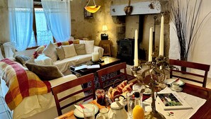 Een gezellige woonkamer met een bank, een ontbijt gedekte eettafel en een open haard.