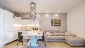 Una cocina moderna con armarios blancos, una campana extractora de acero inoxidable y un comedor con dos sillas.