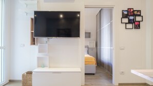 Un dormitorio moderno con una televisión de pantalla plana montada en la pared, una cama con manta a rayas y una mesita de noche pequeña.