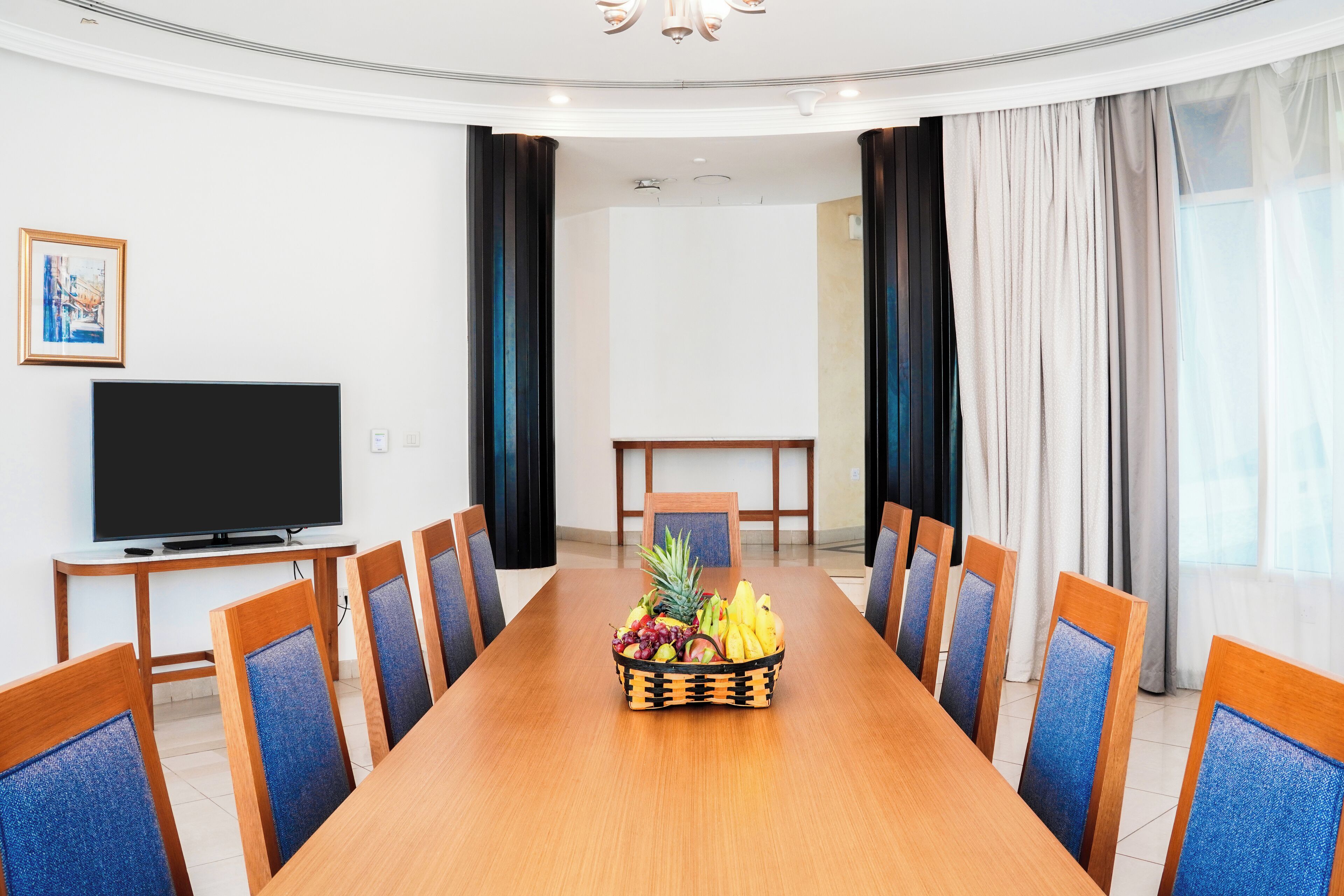 A conference room with a long table, chairs, a television, and a fruit basket.