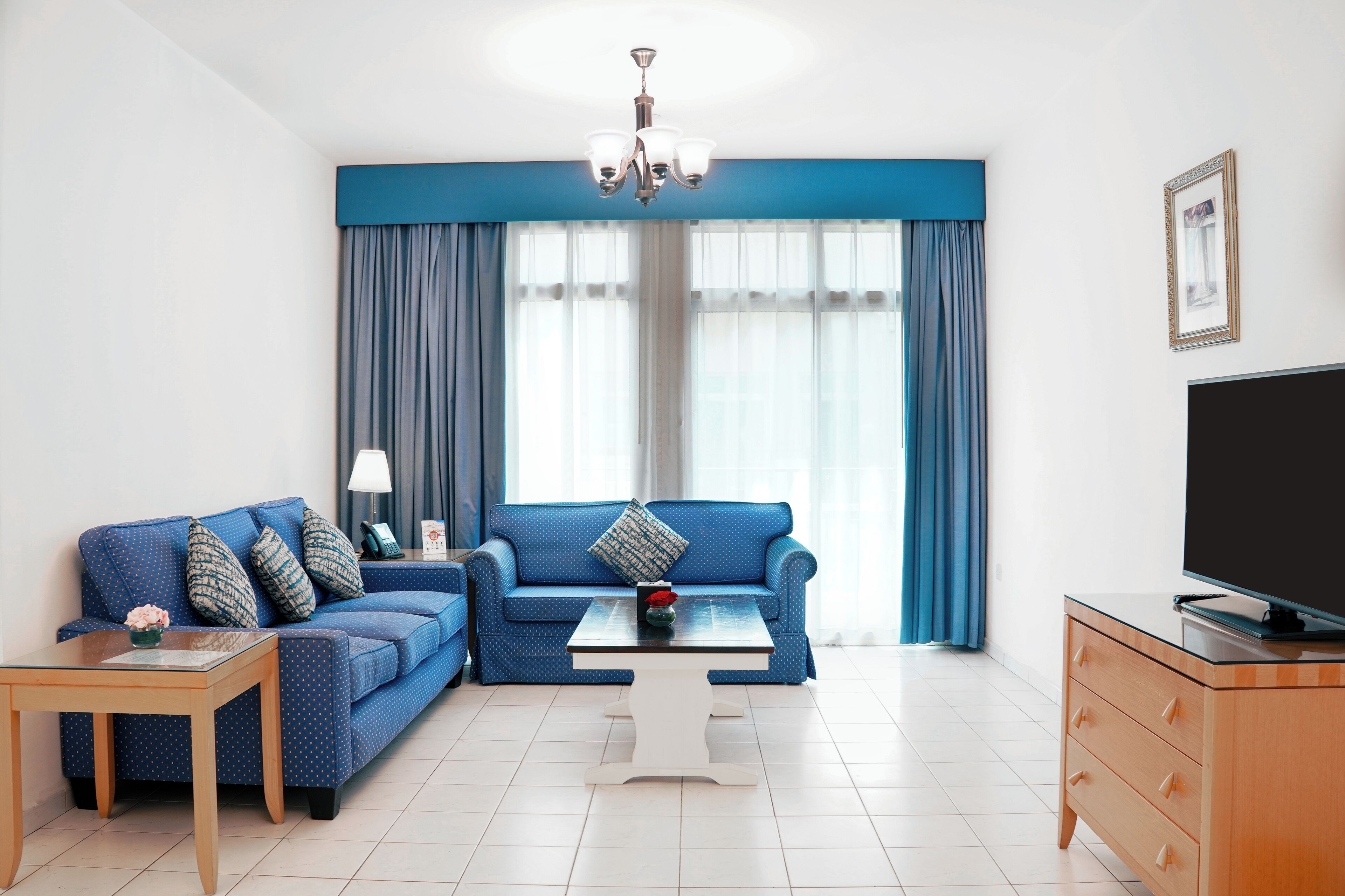 Ein modernes Wohnzimmer mit einem blauen Sofa, einem Couchtisch, einer TV-Konsole und einer Chandelüster.