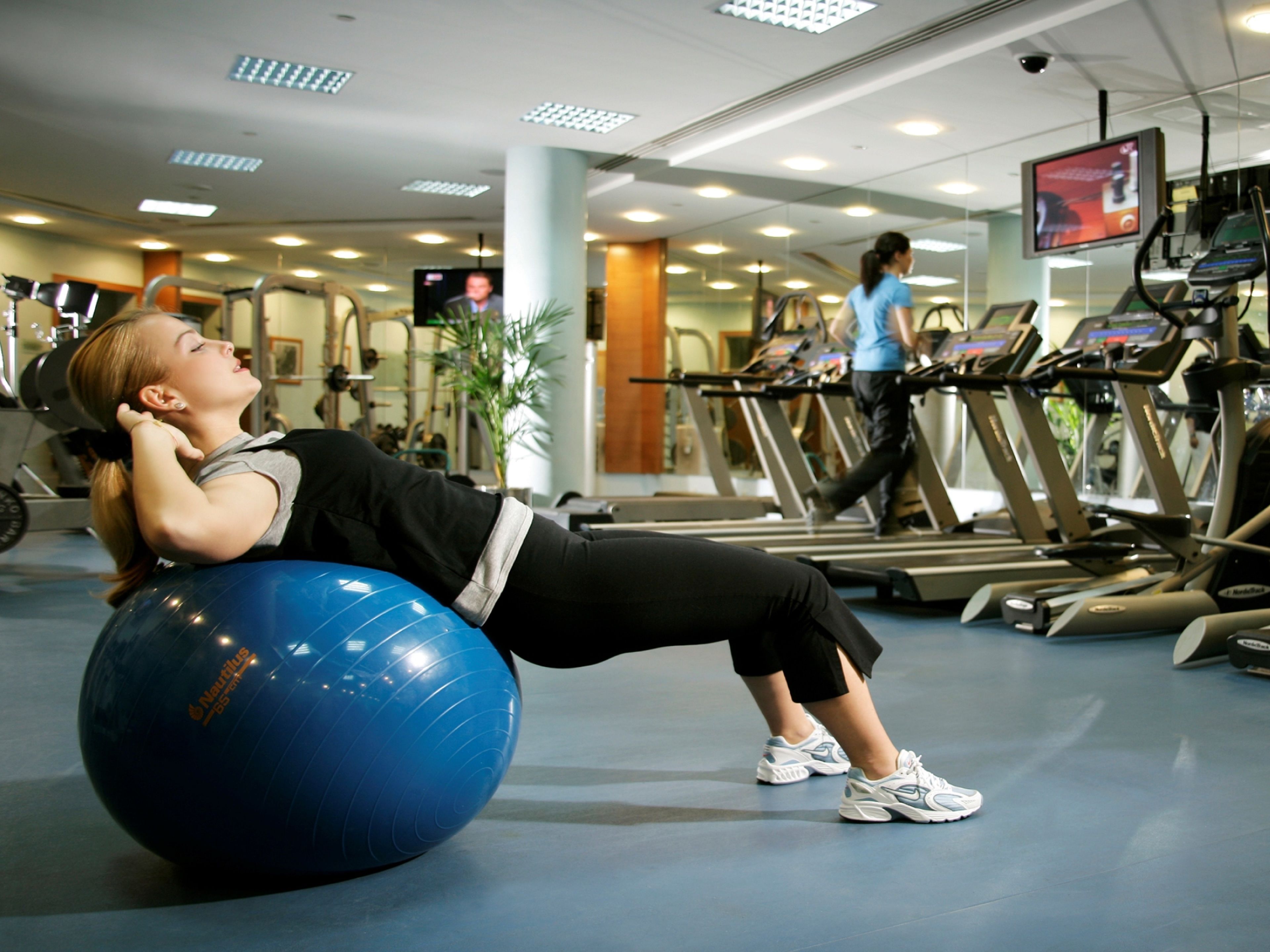 Une salle de sport équipée de matériel d’exercice, notamment un ballon d’exercice bleu et des tapis de course.