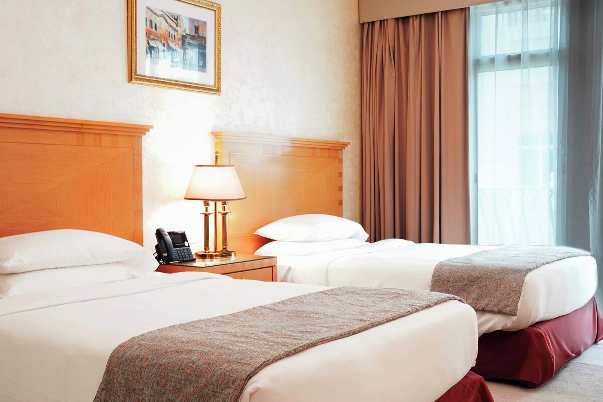 A hotel room with two beds, a nightstand with a lamp, a phone, and a framed picture on the wall.