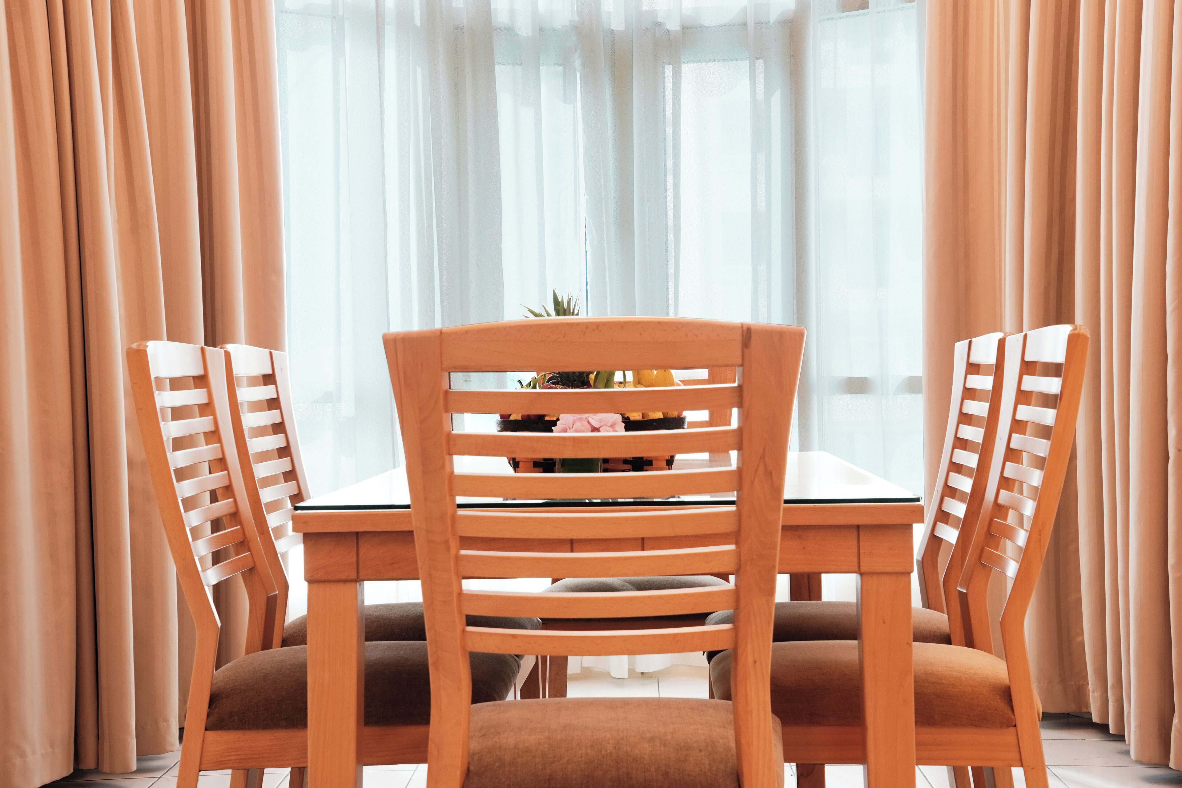 Un coin repas avec une table et des chaises, un vase rempli de fleurs et des rideaux légers.