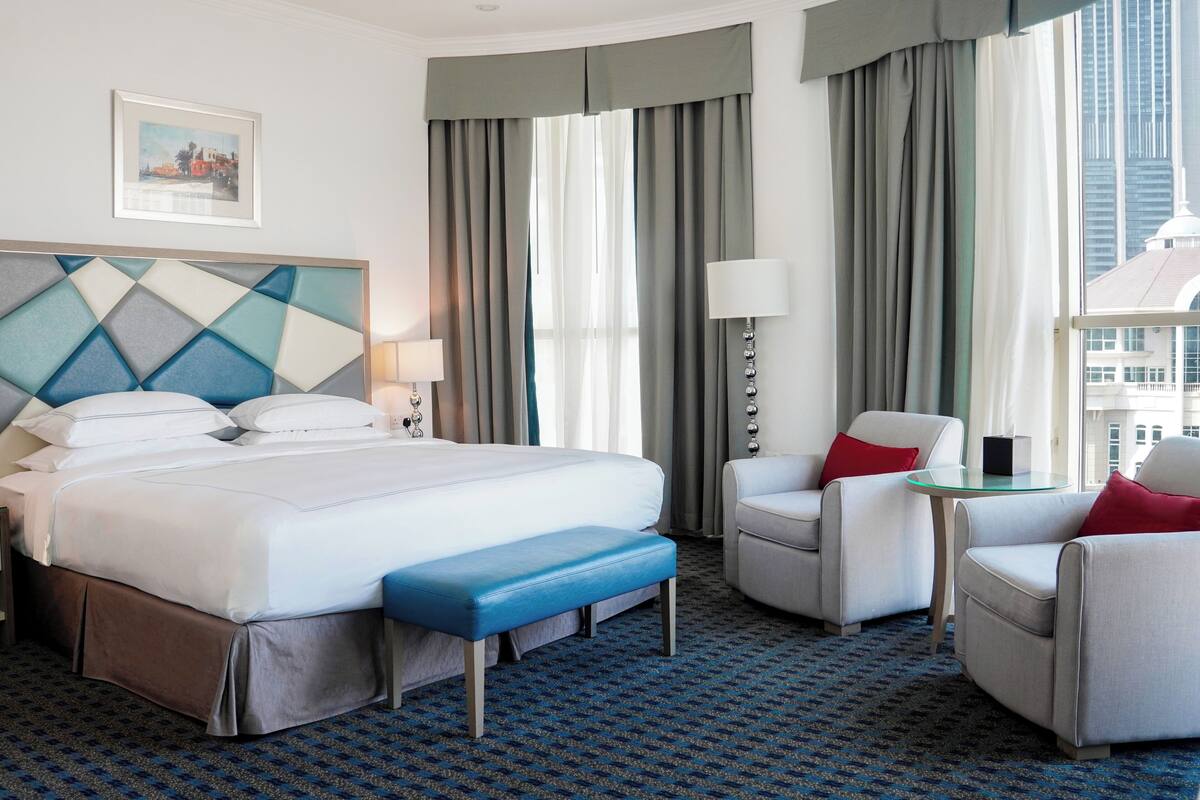 A hotel room with a large bed, two armchairs, a small table, and a bench.
