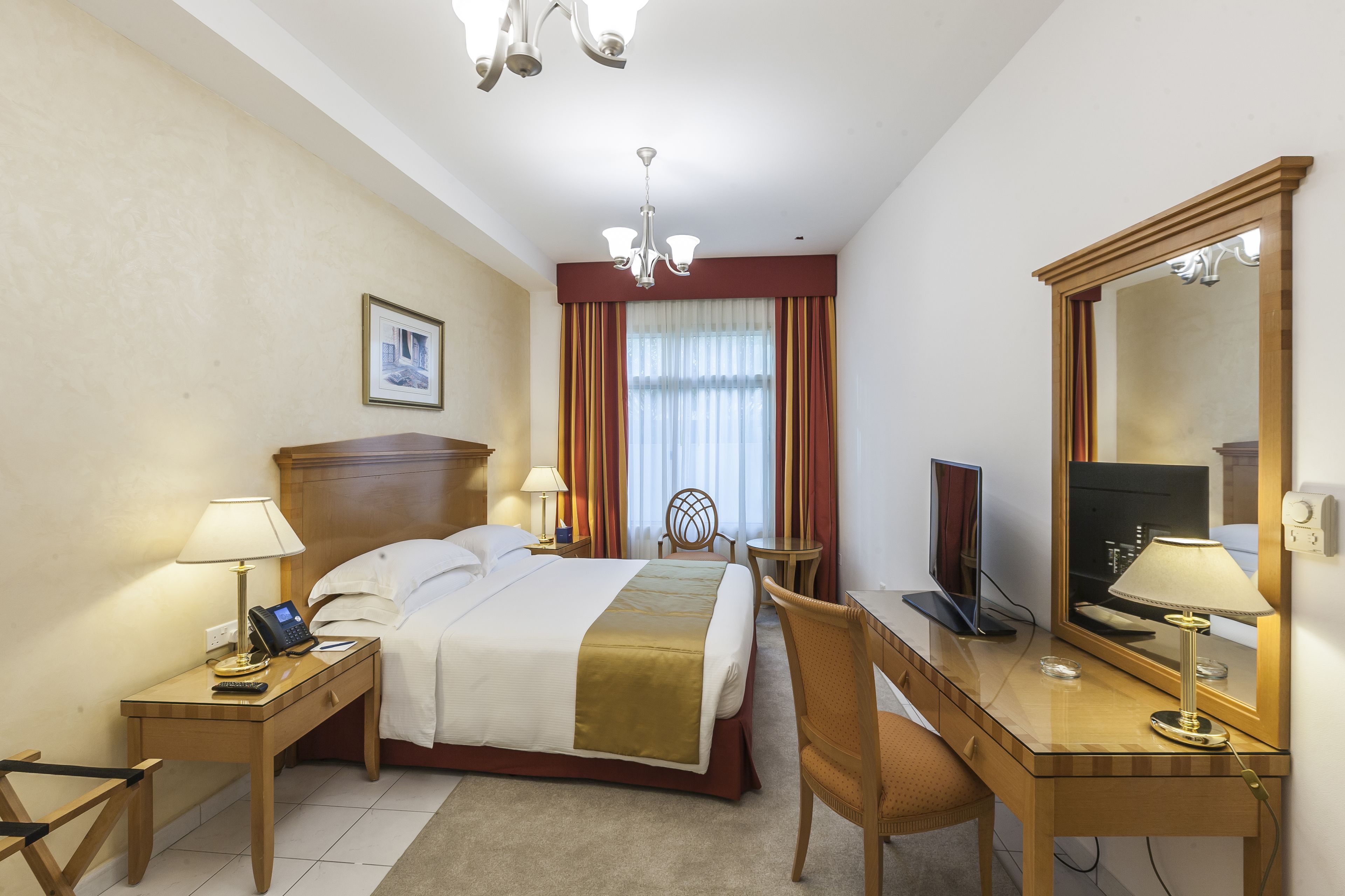 Habitación de hotel con cama, mesita de noche con lámpara, escritorio con silla, televisor y un espejo grande.