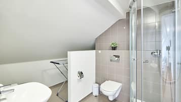 Un baño moderno con ducha envuelta en vidrio, un lavamanos blanco y un inodoro.