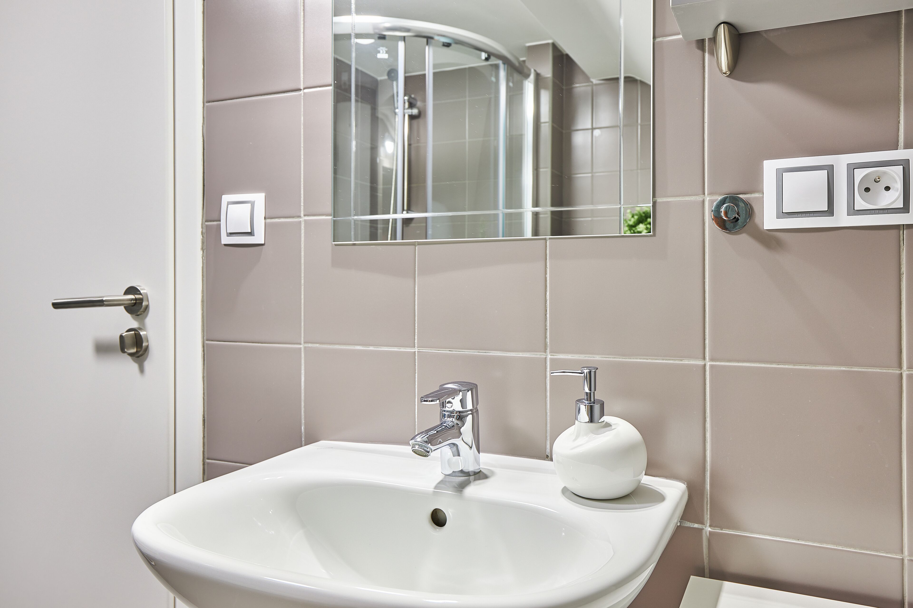 A bathroom with a white sink, chrome faucet, and a soap dispenser.