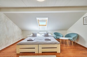 Un dormitorio con cama, dos sillones, una mesita y un tragaluz.