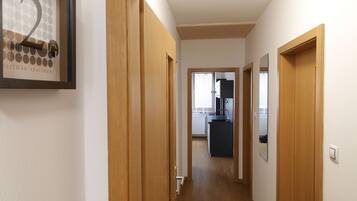 Un couloir avec des portes en bois, un tableau encadré au mur et une horloge.